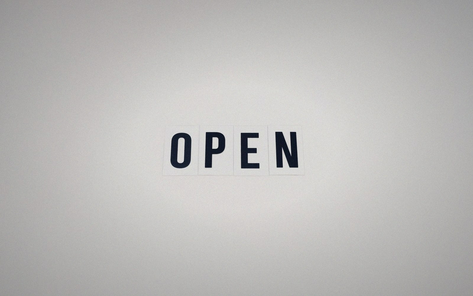 The word "open" spelled out in bold black letters on individual tiles against a plain wall
