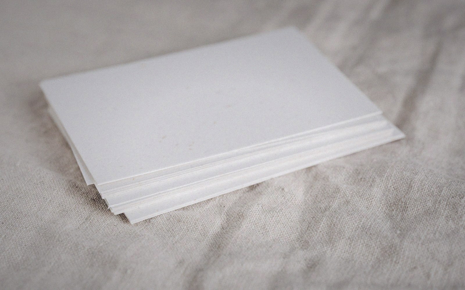 A stack of blank white paper sheets resting on a woven linen surface