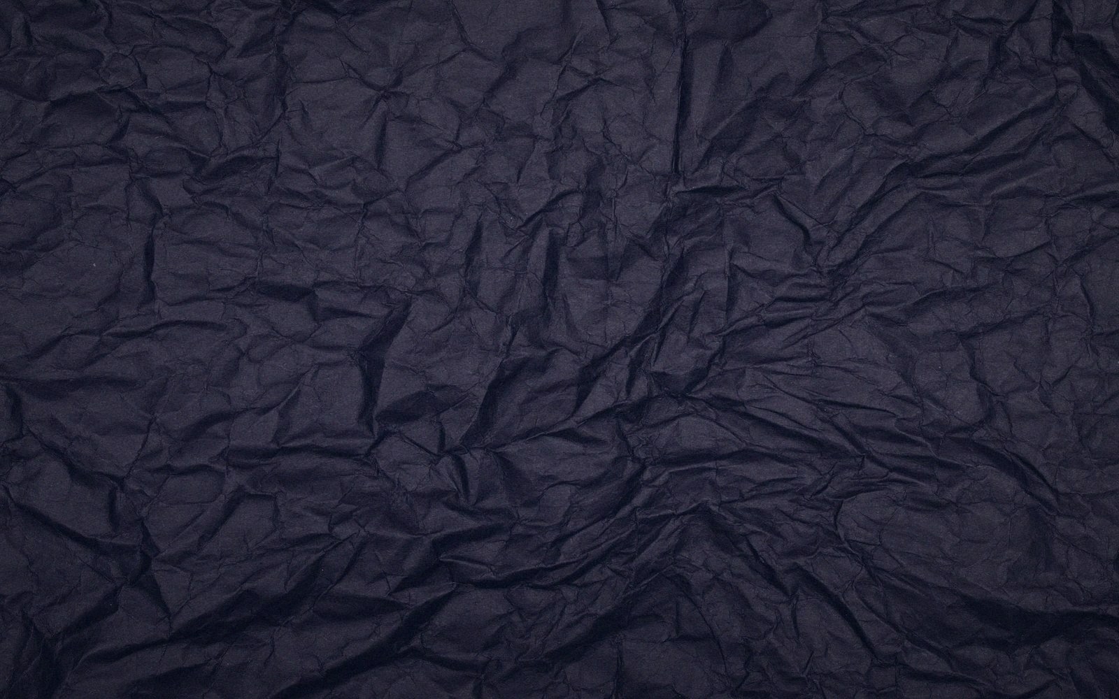 Close-up of dark, deeply wrinkled fabric with folds and creases catching subtle light