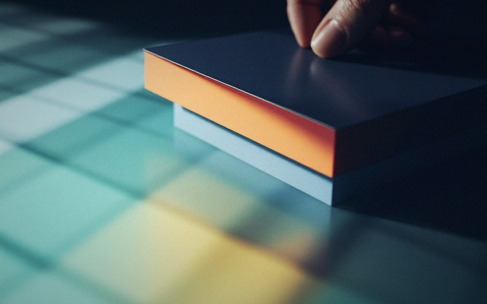 A finger touches the top of a slim card with an orange edge on a colorful surface