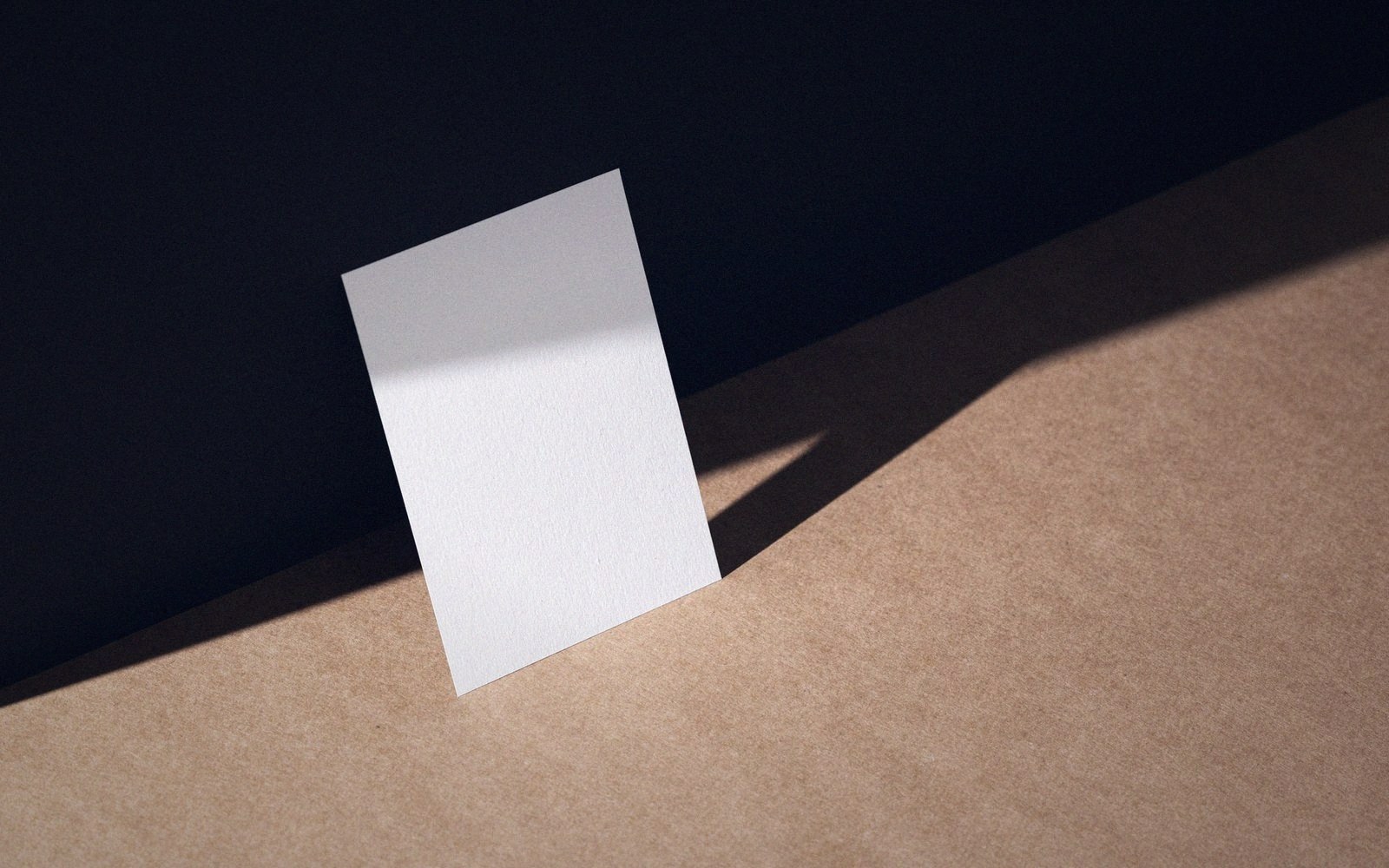 Blank white card standing upright on brown paper against dark background with sharp shadow