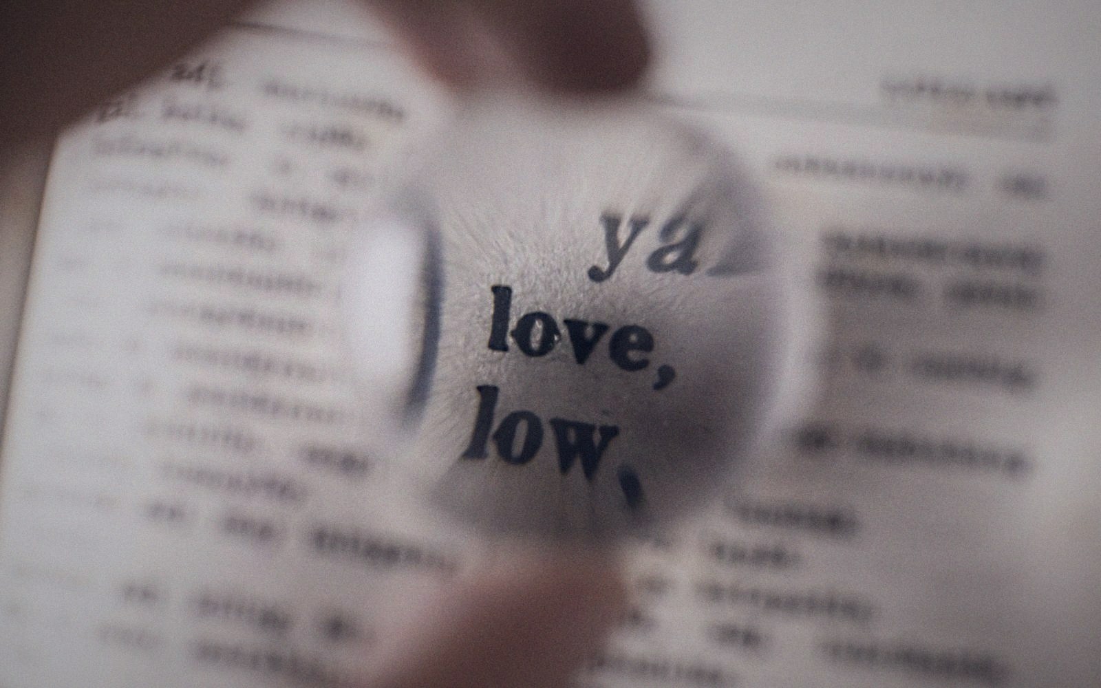 A magnifying glass enlarges small printed text, highlighting the word "love" on a page